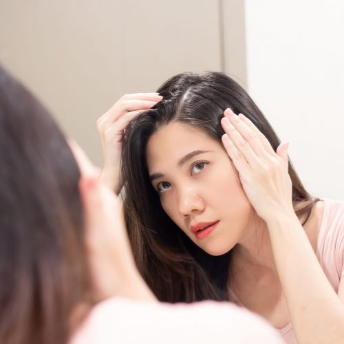 Asian Beautiful woman are looking herself in mirror and use hand touch her hair and looking for  grey hair or hair loss with a worry face.